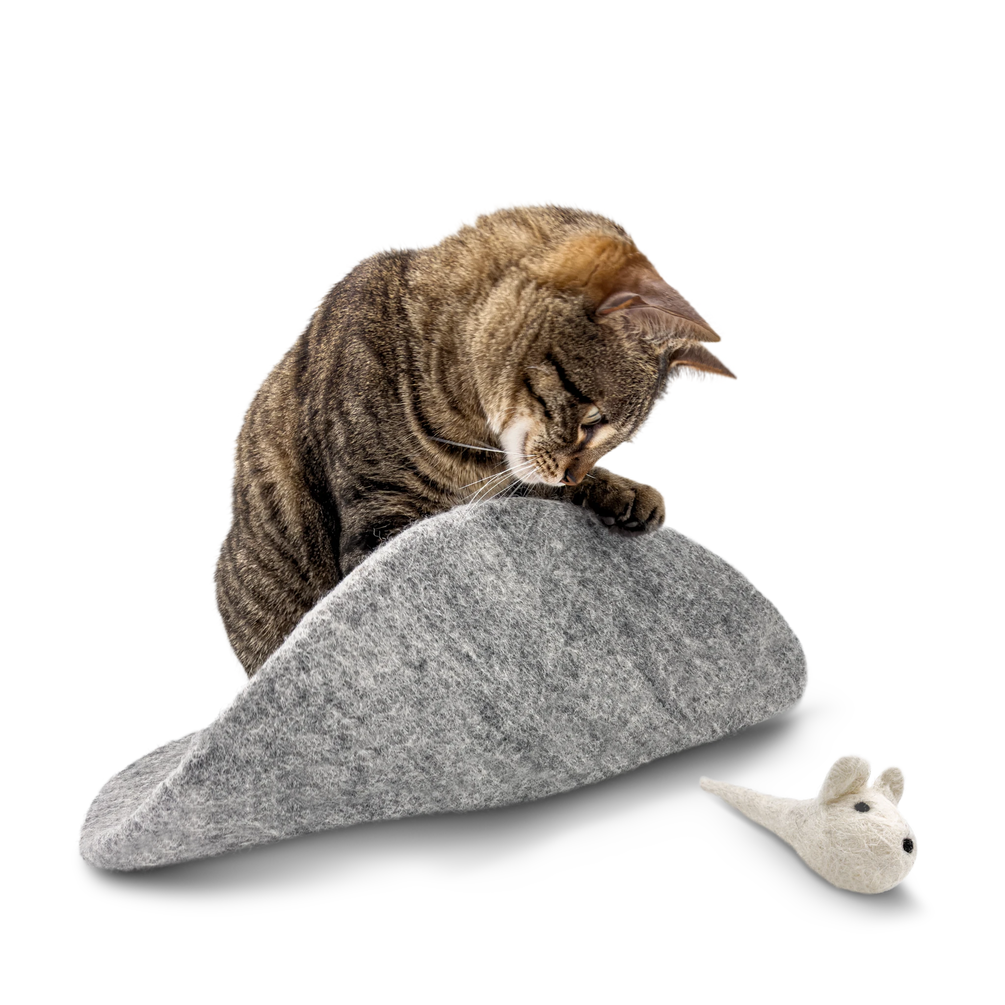 Tabby cat playing with a white felted wool mouse toy on a grey wool mat on a light background.